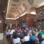Panoramica della sala piena con pubblico di spalle